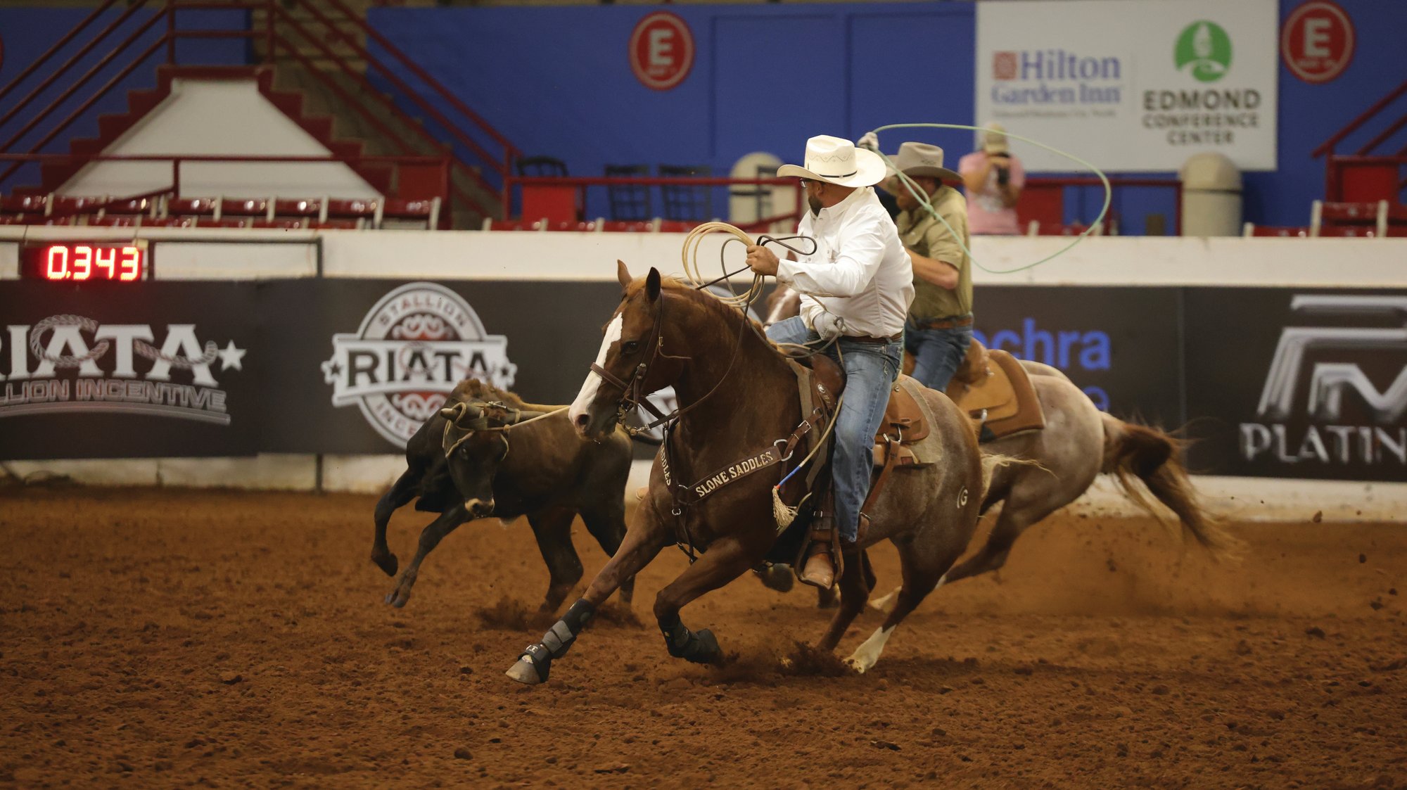 A roper making a run in front of sponsor banners at the Riata Championships