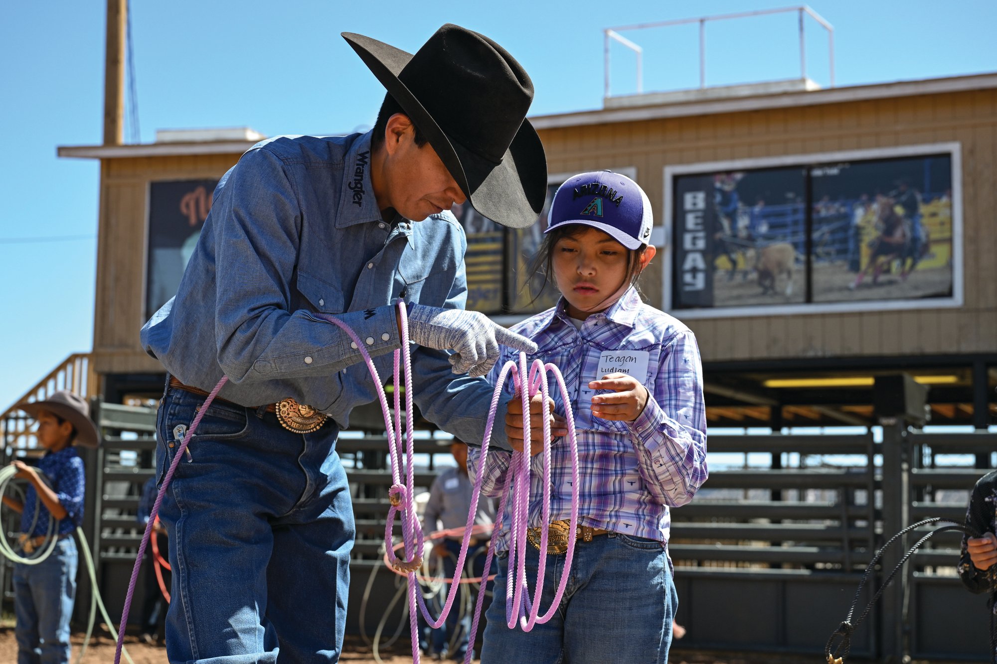 A volunteer instructor helps young roper Teagan Ludlam coil her rope at the free team roping school