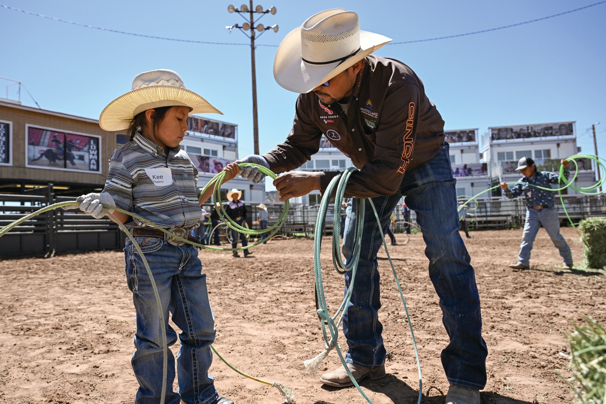 A volunteer instructor helps young roper Kee Platero coil his rope at the free team roping school