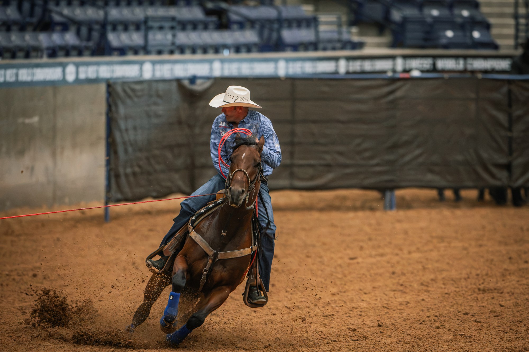 A header in a straw hat and blue plaid shirt turns a bay horse with a red rope dallied at the Old West World Championships in Amarillo, Texas.