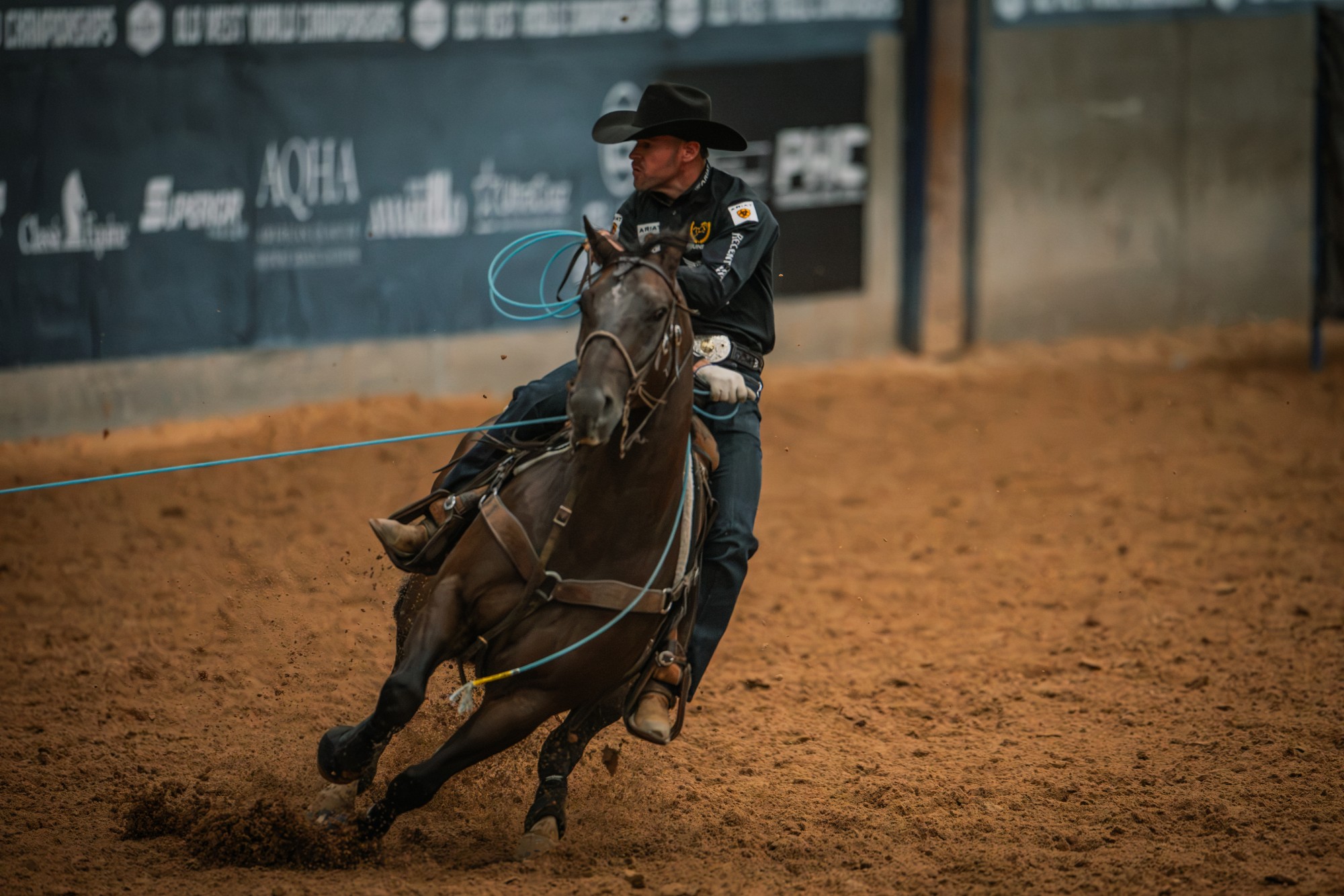 A header in a black hat turns a dark horse in front of Old West World Championships sponsor banners.