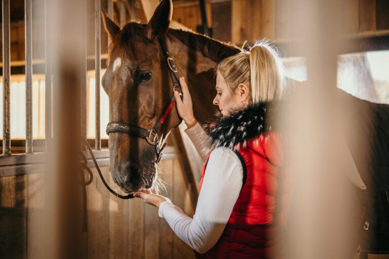 Woman touching and feeding her horse at ranch