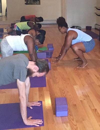 Deanna, Black plus size yoga teacher leads her students in a pose.