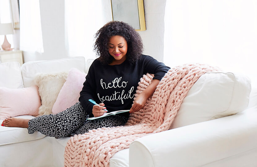 woman writing in journal in plus size athleisure and sitting on couch