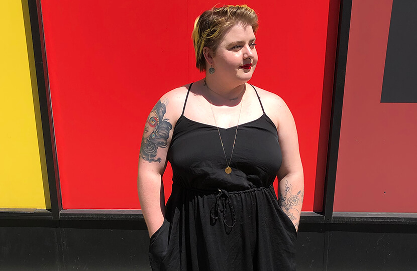 tattoos nikki bosso standing in front of red wall in black dress