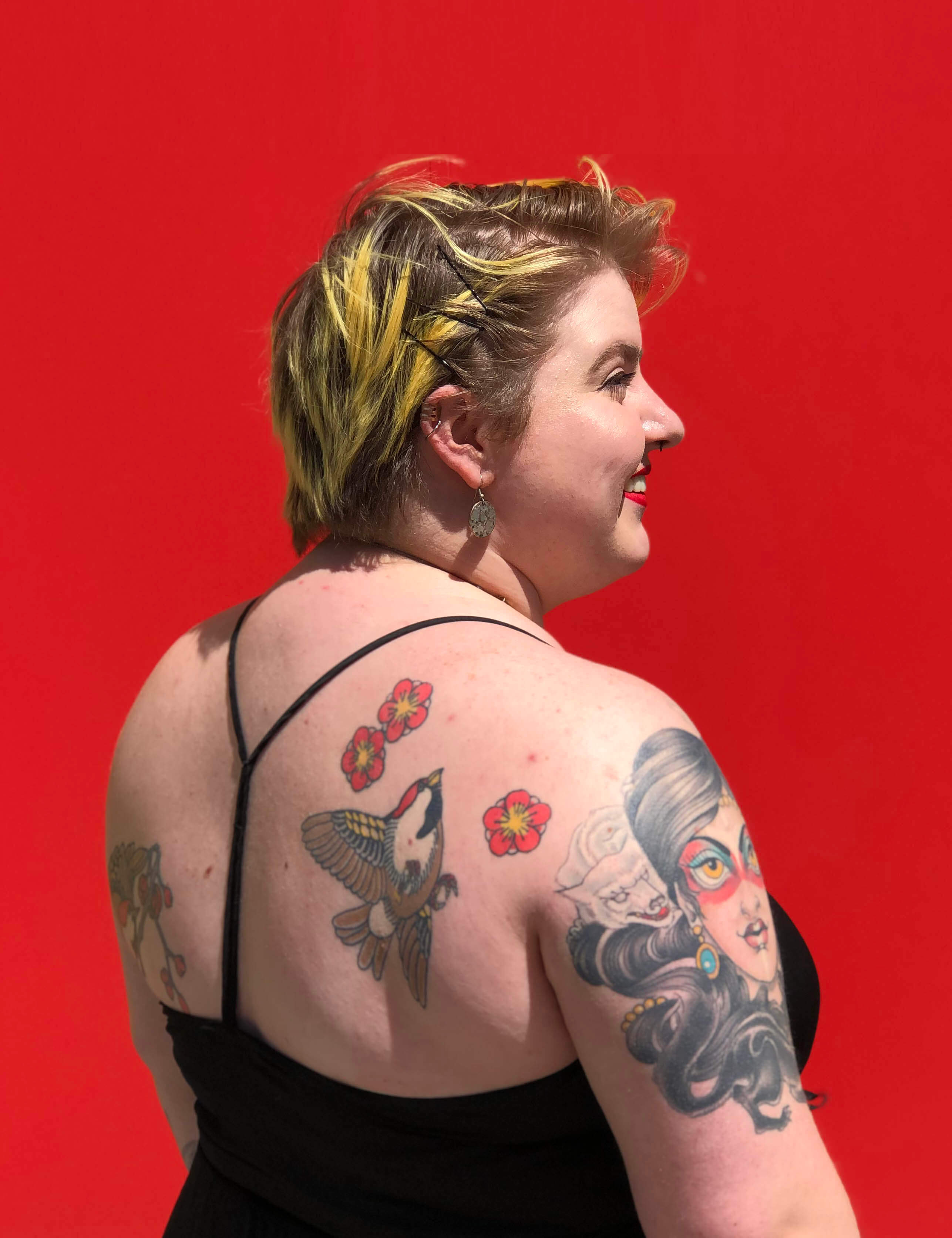 nikki bosso showing off tattoos on her back in front of red wall