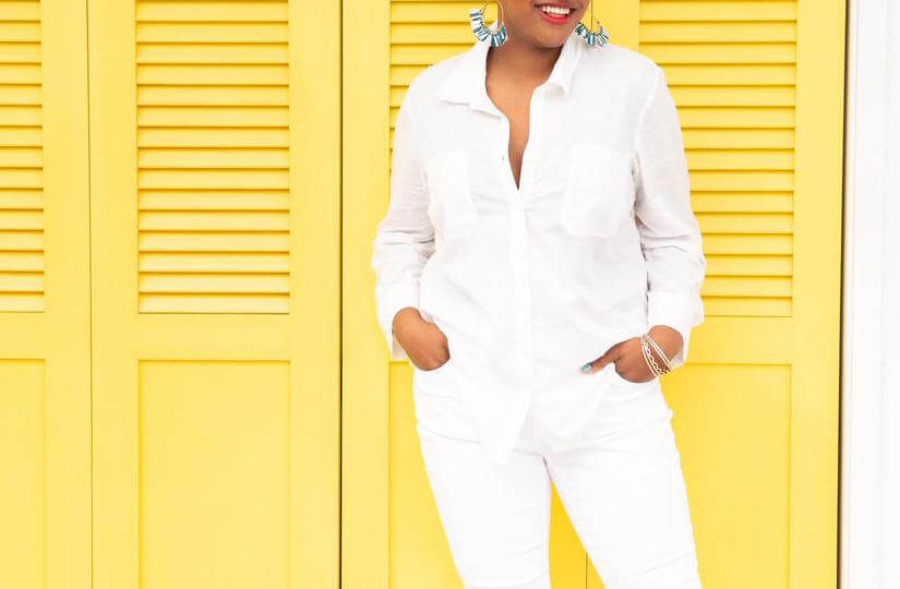 plus-size model wearing a white top and white jeans with bold jewelry.