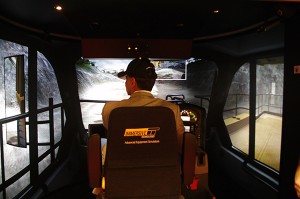 Minister Virk checks a side mirror while operating the haul-truck simulator.