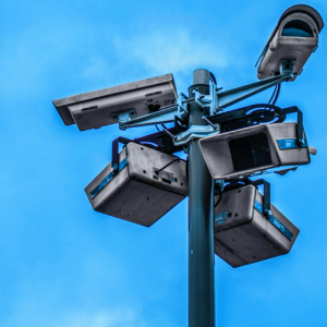 surveillance cameras pointing in every direction from the top of a pole, with the blue sky visible in the background.