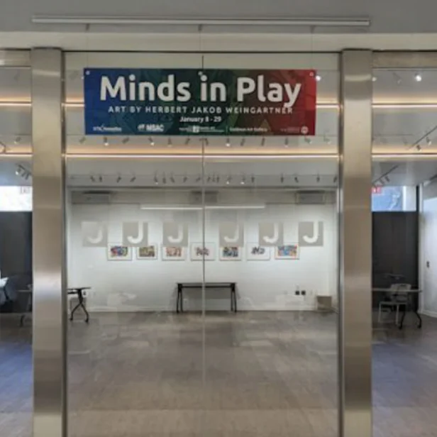 Art gallery entrance displaying a sign that reads "Minds in Play: Art by Herbert Jacob Weingartner." Framed artwork is visible on the walls inside the gallery.