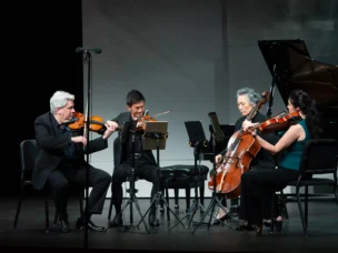 A string quartet performs on stage with two violinists, a cellist, and a violist, dressed in formal attire.