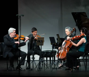 A string quartet performs on stage with two violinists, a cellist, and a violist, dressed in formal attire.