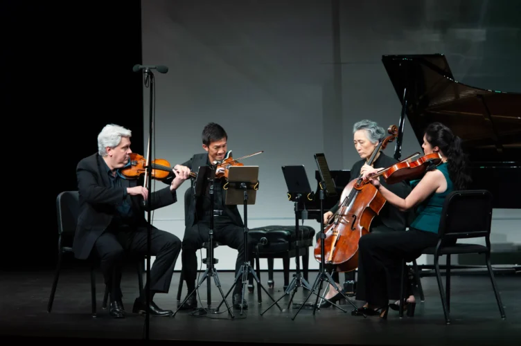 A string quartet performs on stage with two violinists, a cellist, and a violist, dressed in formal attire.