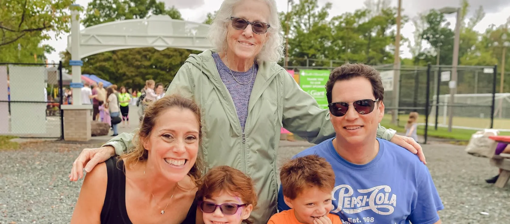 An elderly woman posing outside behind a man, woman, and two young boys.