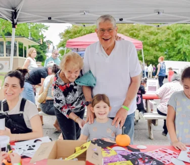 An elderly couple posing with a little girl at a craft table.