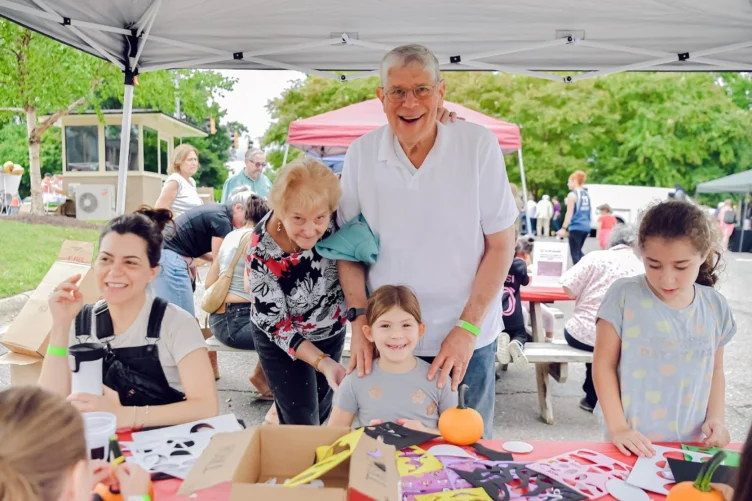 An elderly couple posing with a little girl at a craft table.