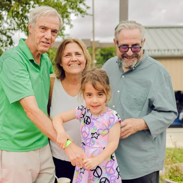 An older woman and two men pose for a photo with a little girl in a dress with peace signs, stars, and hearts.
