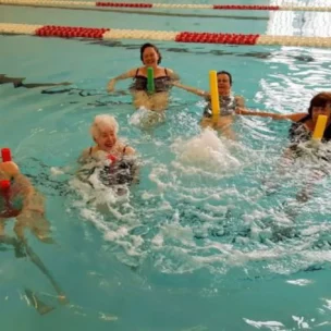 A group of adults in an indoor pool using pool noodles.