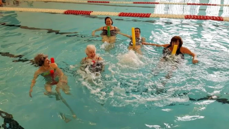 A group of adults in an indoor pool using pool noodles.