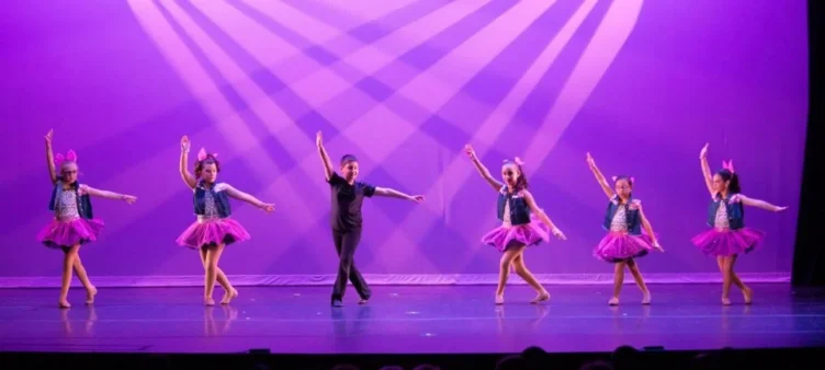 Five young girls and a boy in the middle posing onstage in costumes.