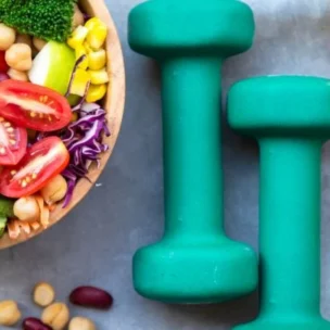 A healthy bowl of salad with dumbbells and a measuring tape.
