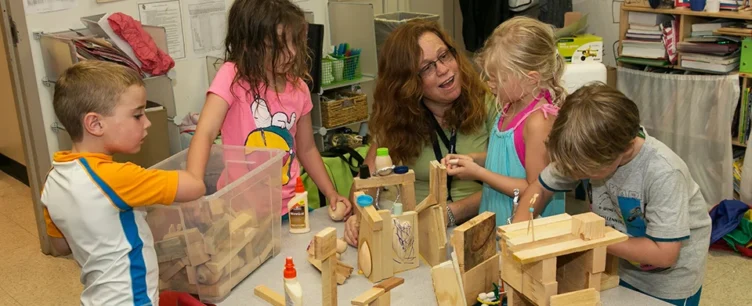 An instructor or mentor with four children playing with wooden blocks.