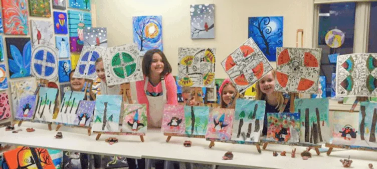 Six children posing in an art room holding up their paintings.
