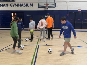 Participants in Shavim Soccer kicking soccer balls in the gym.