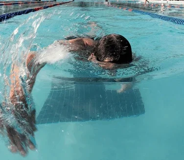 A swimmer performs freestyle in a lane of an outdoor swimming pool, with one arm extended forward and the face partially submerged in the water.