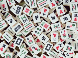 A scattered pile of Mahjong tiles with various Chinese characters, symbols, and patterns in red, green, and black on a white background.