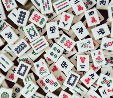 A scattered pile of Mahjong tiles with various Chinese characters, symbols, and patterns in red, green, and black on a white background.