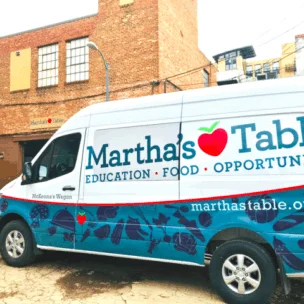 A Martha's Table delivery van is parked outside a brick building, displaying the organization's name, website, and the words "Education • Food • Opportunity.