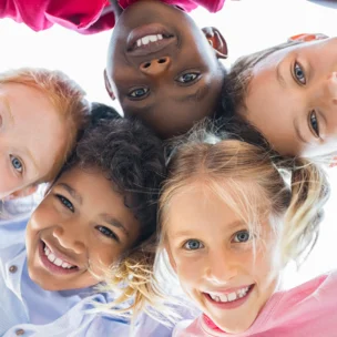 Five children smiling and looking down at the camera, standing close together in a circle with their heads touching.