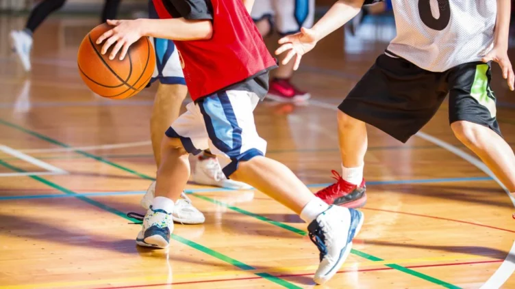 Children playing basketball indoors, focusing on their legs and the ball as one player dribbles while being guarded by others.