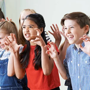 A group of children stand indoors making playful claw gestures and fierce faces, appearing to pretend to be monsters or animals.