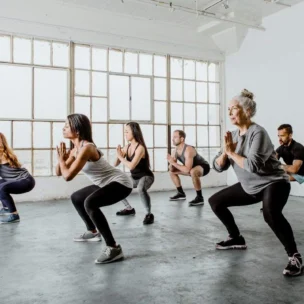 A group of people in athletic wear performing squats in a bright, spacious room with large windows.