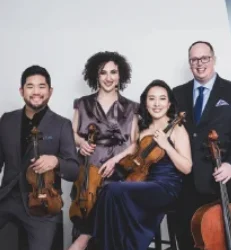 Four formally dressed musicians pose together with string instruments against a plain background.