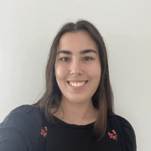A young woman with long brown hair, wearing a black top with small red floral details, smiles in front of a plain white background.