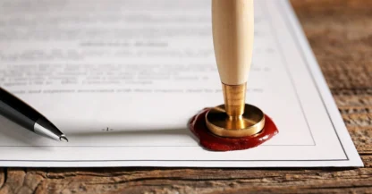 A document on a wooden table is sealed with red wax and a stamp; a black pen lies next to it.