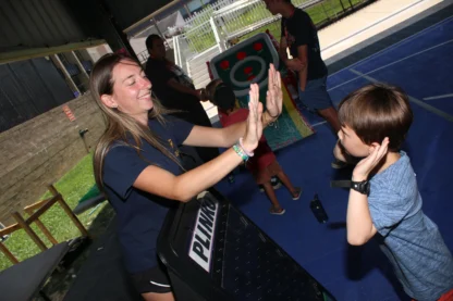A young woman and a child give each other a high-five at an indoor recreational area with game equipment and other people in the background.