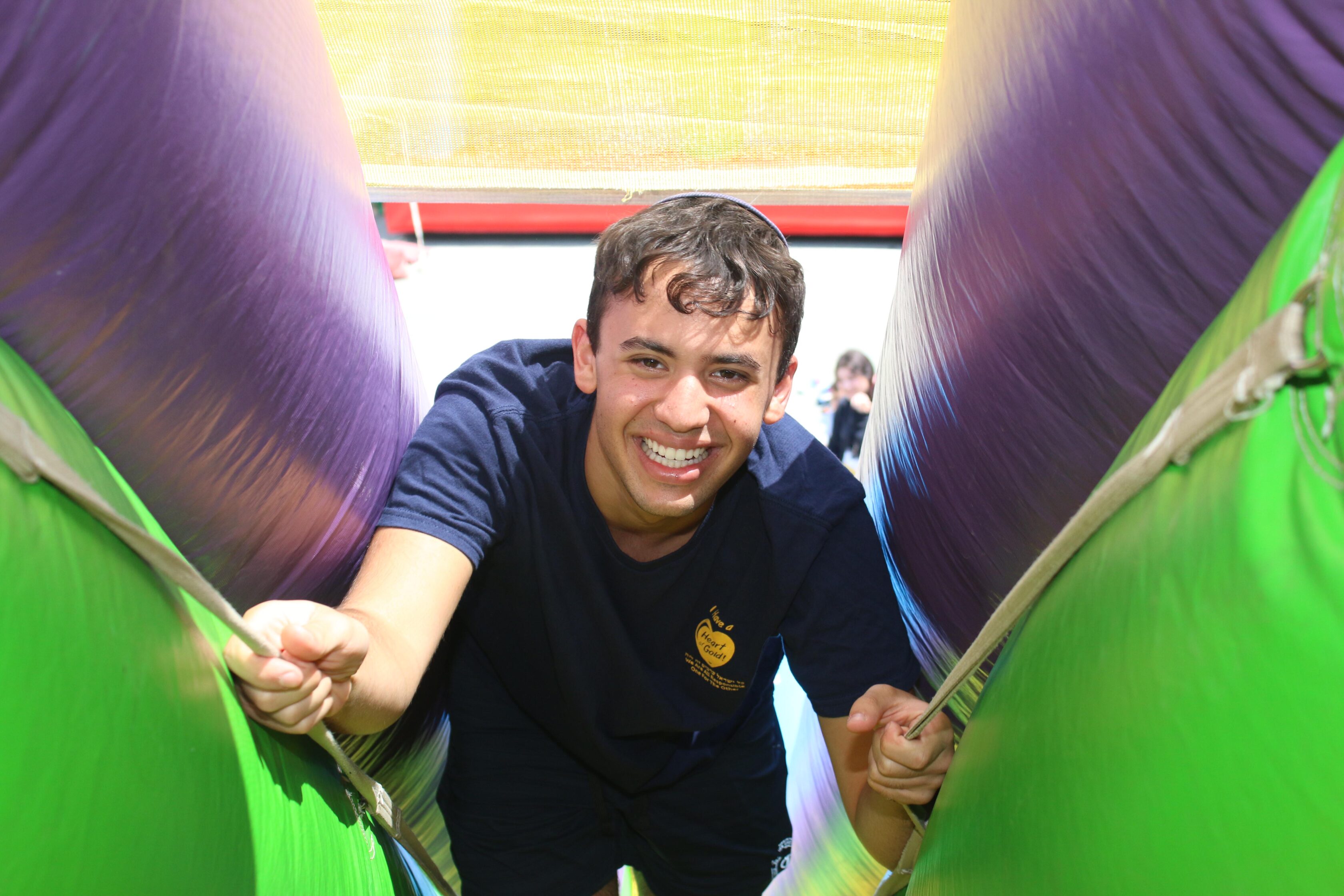 A young man in a navy blue shirt climbs an inflatable obstacle course, smiling at the camera.
