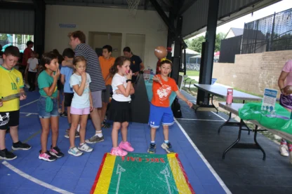 Children participate in a football toss game at an indoor event, with one boy throwing a ball while others watch and wait their turn.