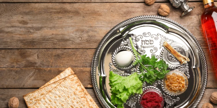 A Passover Seder plate with traditional symbolic foods, matzah, walnuts, and a bottle of wine on a wooden table.