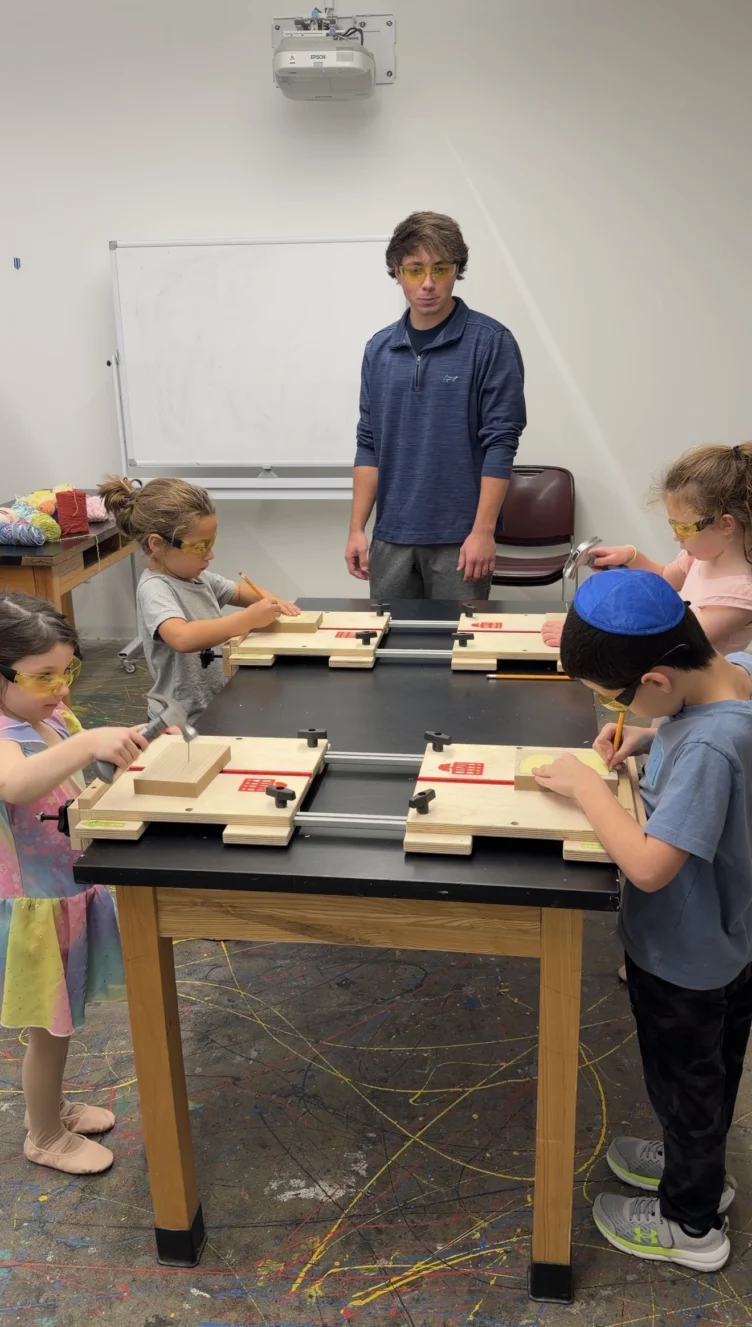 A group of young children work on woodworking projects at a table while an adult supervises in a classroom setting.
