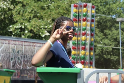 A young woman with braided hair and sunglasses makes a peace sign while sticking out her tongue on an amusement park ride.