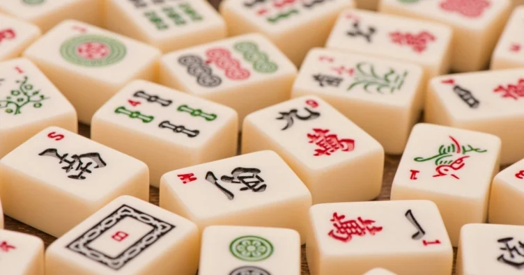 A close-up of ivory-colored mahjong tiles scattered together, each featuring unique red, green, and black engraved symbols.