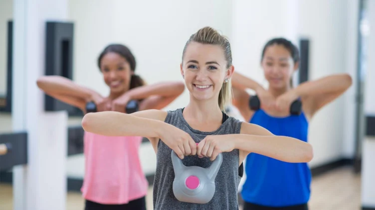 Three women exercising with kettlebells in a gym.