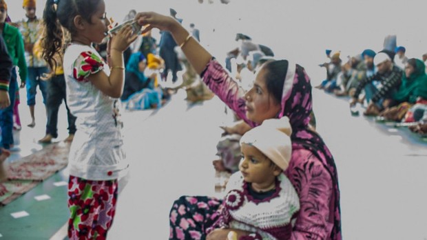 A mother holds a bowl of water for her daughter to drink from in the main eating hall of the langer. Photo by Hán Zhang.