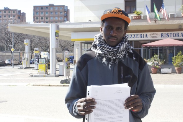 The chill of winter in northern Italy has warmed into a summery March day at the abandoned Olympic Village in Turin, where Amadou Jallow, 29, is outside squinting and smiling brightly in the sun. He’s holding the story of his journey from Africa to Italy, which he typed inside an Italian refugee camp.   Originally from Gambia, Jallow left the country in 2009 and travelled throughout northern Africa before reaching the Sahara Desert. For three days, he walked through the desert by foot. The heat was scorching and many other travelling migrants were killed by dehydration. “In my life, I never see dead bodies like this — maybe only on TV or something else,” he said of seeing dead bodies on the sands of the Sahara.   Once in Libya, Jallow settled and found work in construction. But his time there was cut short by the uprising that same year, in 2011. That year, the civil war and overthrow of brutal dictator Muammar Gaddafi left at least 30,000 dead, according to estimates from the country’s former health ministry. Throughout the bloodshed, black Africans like Jallow faced discrimination and violence from other Libyans, he said.   “They said the blacks are the ones helping Gaddafi,” he said. “So if they see you are black, they will kill you.”   Within months, Jallow fled Libya and crammed into a boat with other migrants. They ended up in the Mediterranean Sea, off the coast of Lampedusa, Italy. An Italian rescue team saved him and others, taking them to a Red Cross camp in nearby Bari.   Jallow now lives at the abandoned Olympic Village in Turin, where he finds resources like schooling and food through the organization of students and local residents that serves the village’s residents — Ex Moi. A Muslim, he said he lives in peace among the other religions and ethnicities at the village. And he’s grateful for them, the volunteers’ help, and for his own survival of a trans-continental journey.   “The things I pass by — I see my people die, but I don’t die,” he said. “So I say, ‘Thank God.’”   Still, he struggles to find a regular job in Turin. He has only found an occasional gig selling newspapers. It pays 25 euros a day for about nine to 10 hours of work.   “I like Italy but the problem is no work,” he said. “I’m here four years now and never work in Italy.”   