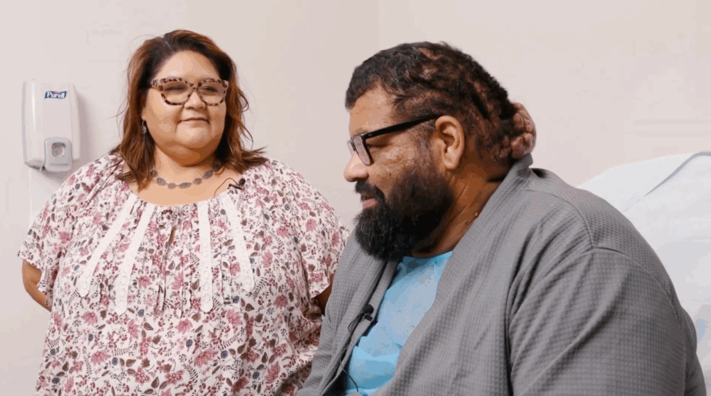 John sits next to his sister in a hospital room. His sister came on the day of his surgery to offer support.